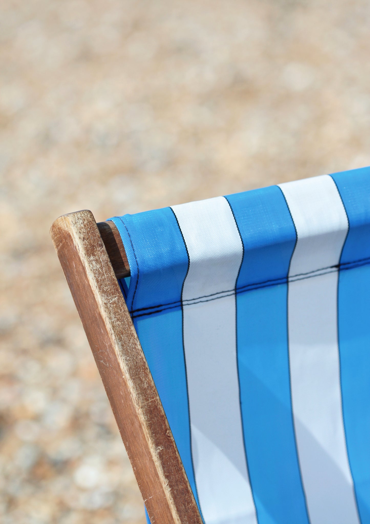 Close-up image of a deck chair, blue, white striped and brown.